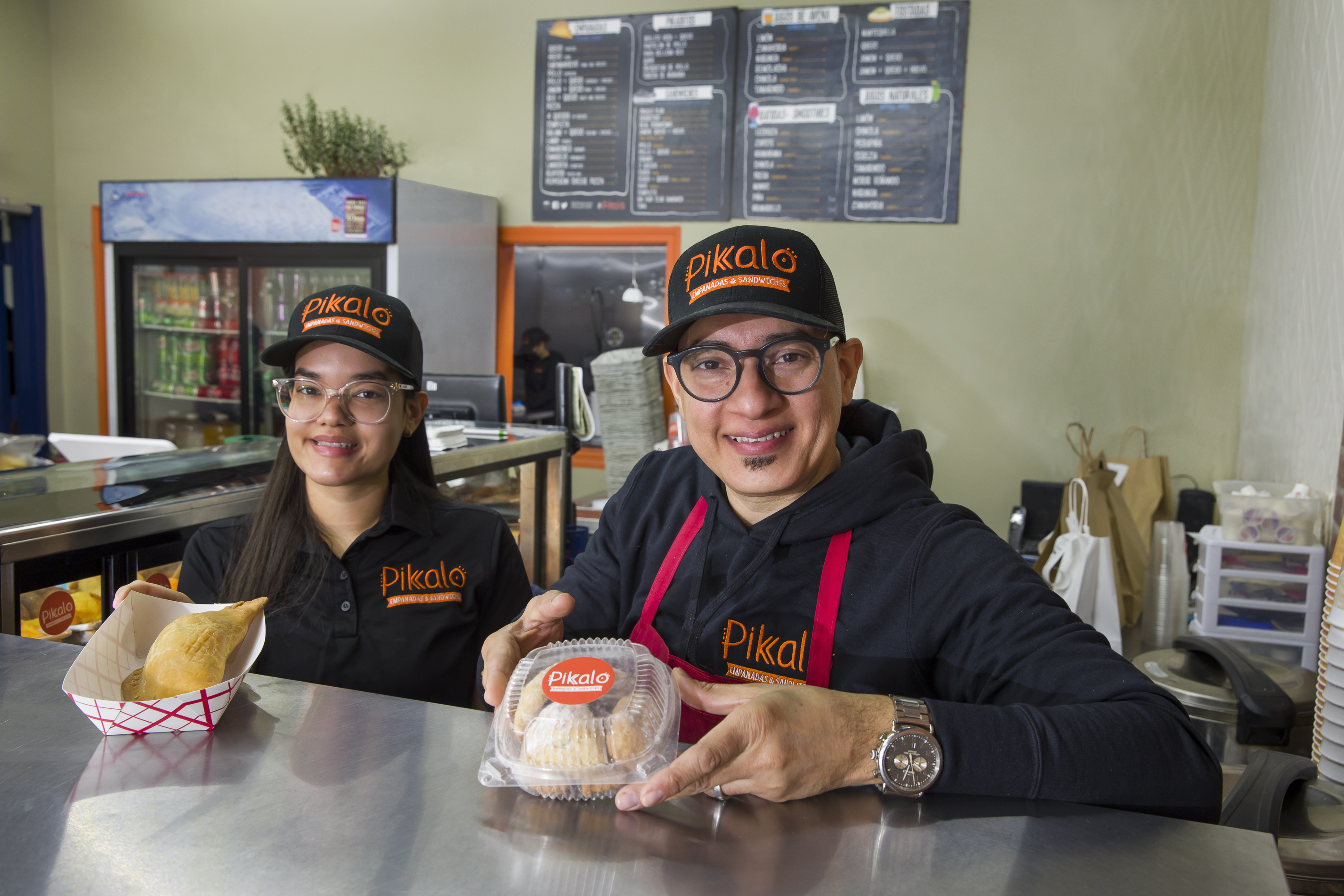 Pikalo owner Jose Pimentel stands with a woman employee behind a counter holding empanadas