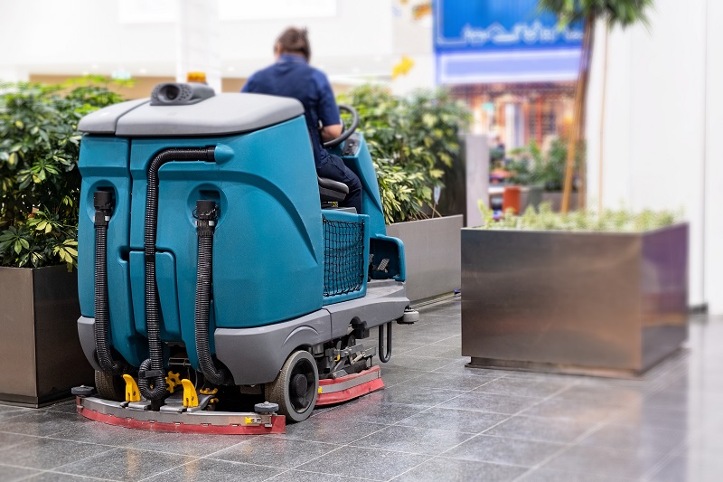 A person drives a floor cleaning machine in the courtyard of a shopping center
