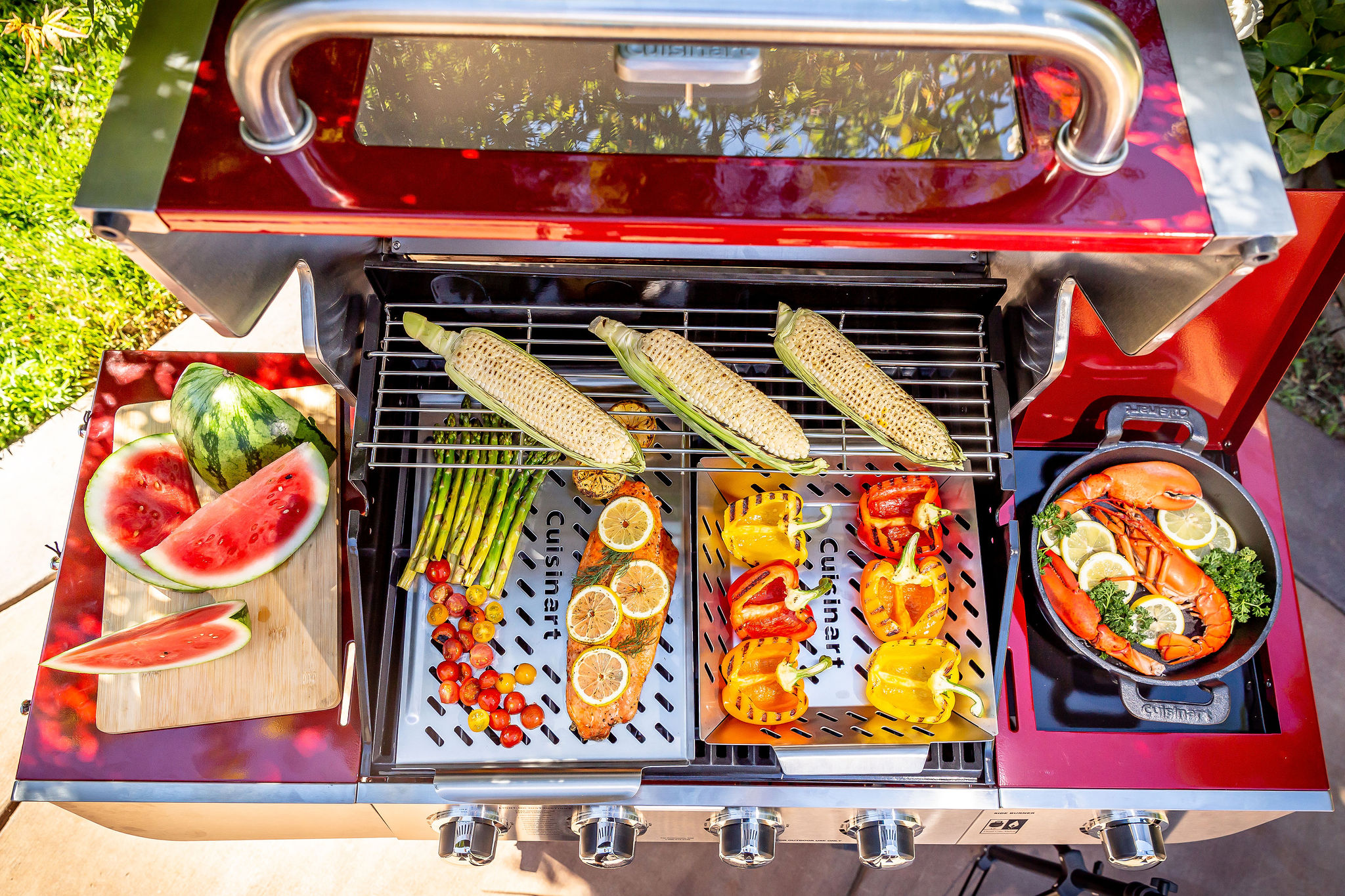 An open grill showcases a variety of grilled food including corn, peppers, salmon, and asparagus with a side of watermelon