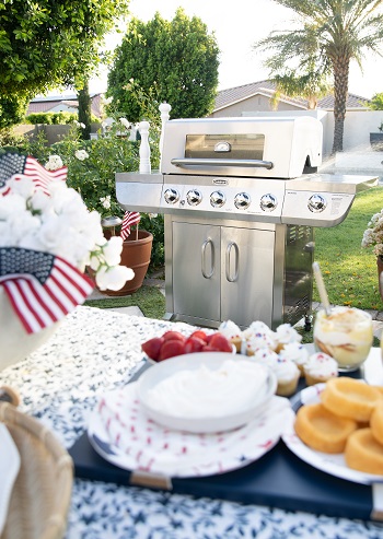 A grill sits in the background while the foreground displays a picnic table with dessert 