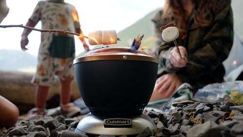 A small portable fire pit sits on rocks and roasts a marshmallow held over its flame by a stick