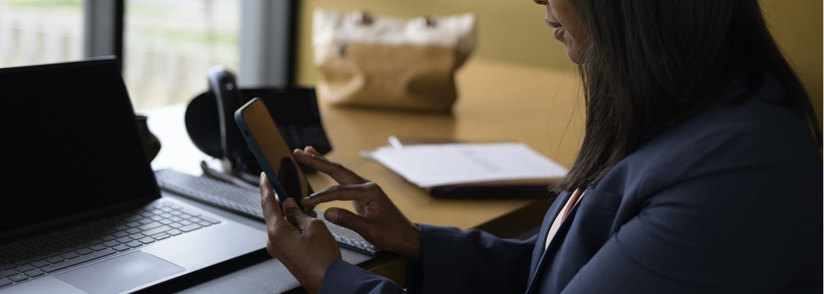 A woman sits at her desk and upgrades her online banking mobile app on her phone