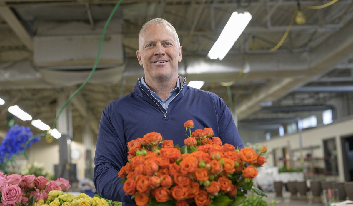 Ted Winston wears a blue sweater and holds a bushel of orange flowers