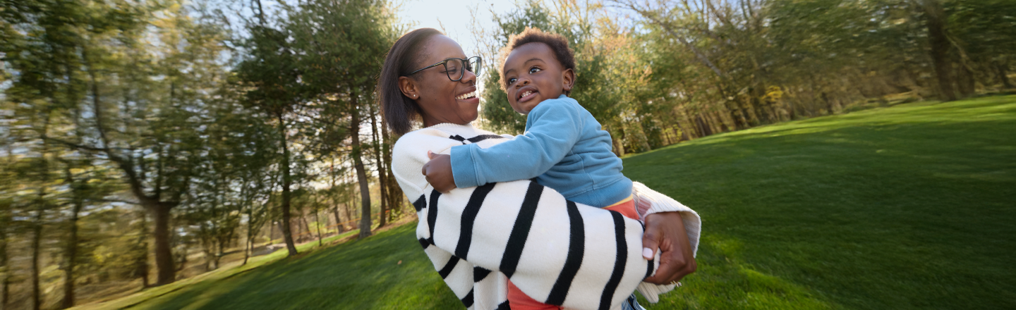 A happy mother holds her young son in her arms in a park