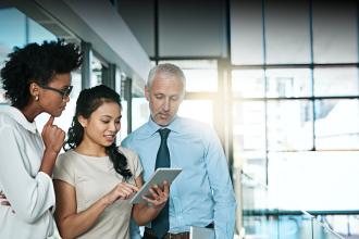 Two women and a man gather around a tablet to review their commercial business plan