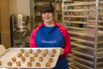 Collette Divitto stands in the kitchen of her bakery holding a tray of cookie dough ready to be baked