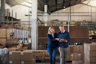 Business owners stand in their company's warehouse and review financial info on a tablet
