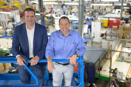 Owners of Gemline stand on a crane overlooking warehouse