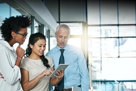 Two women and a man gather around a tablet to review their commercial business plan