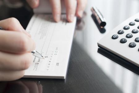 A person writes out a check in a checkbook on top of their desk