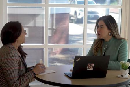 Two women sit at a table with a laptop and discuss business objectives
