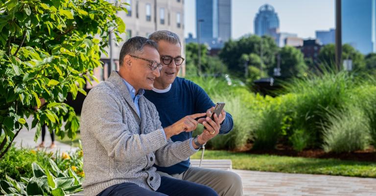 A couple sits outside and reviews checking account options on their mobile phone