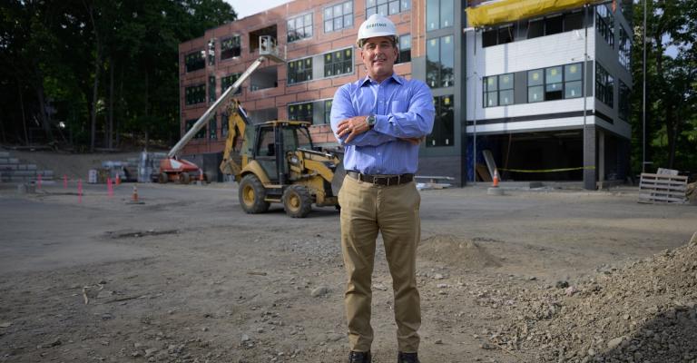 A man stands outside of a construction site wearing a helmet