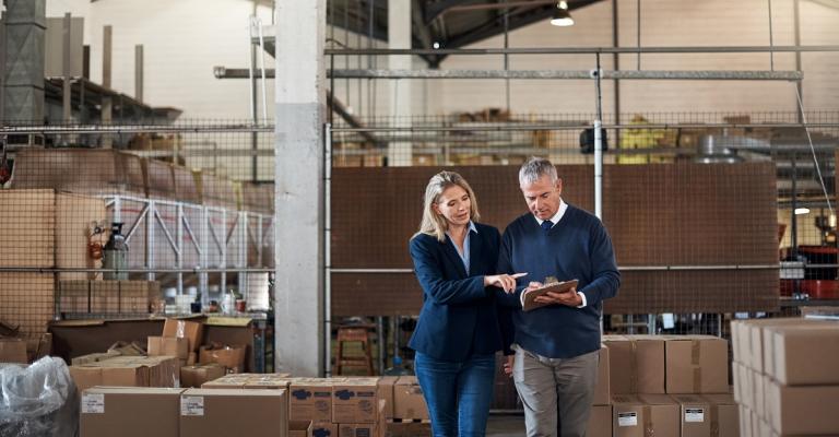 Business owners stand in their company's warehouse and review financial info on a tablet