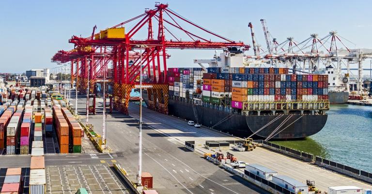 A photography view of a dock in a wharf with a large cargo ship stacked with shipping containers