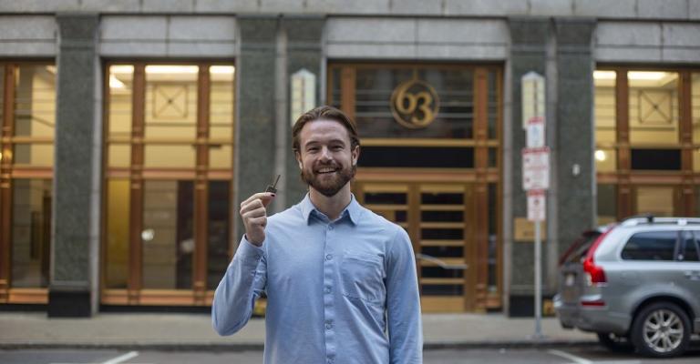 Connor Schoen stands in front of a building in Boston and holds up the building key
